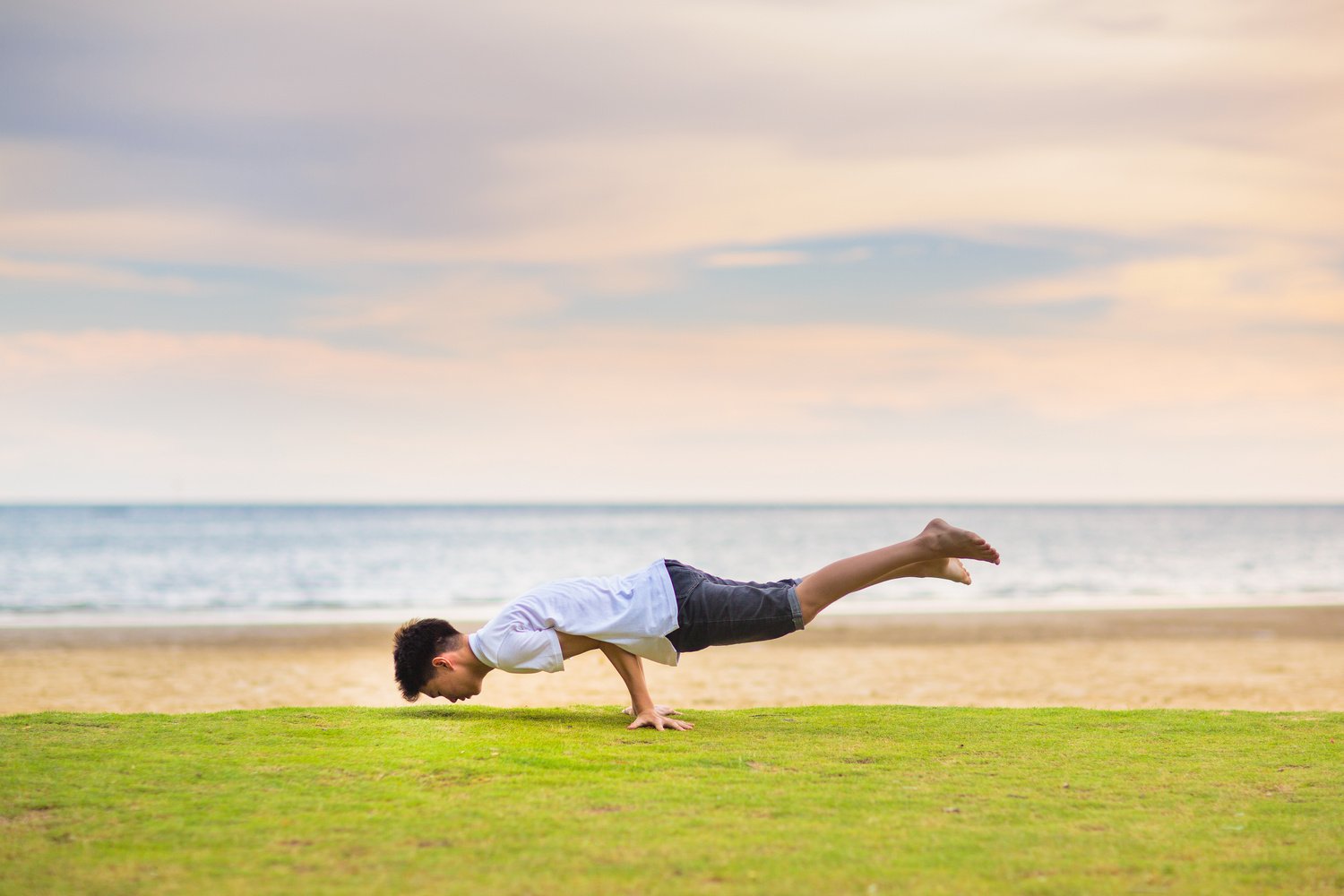 Teenager doing calisthenics exercise. Beach yoga.